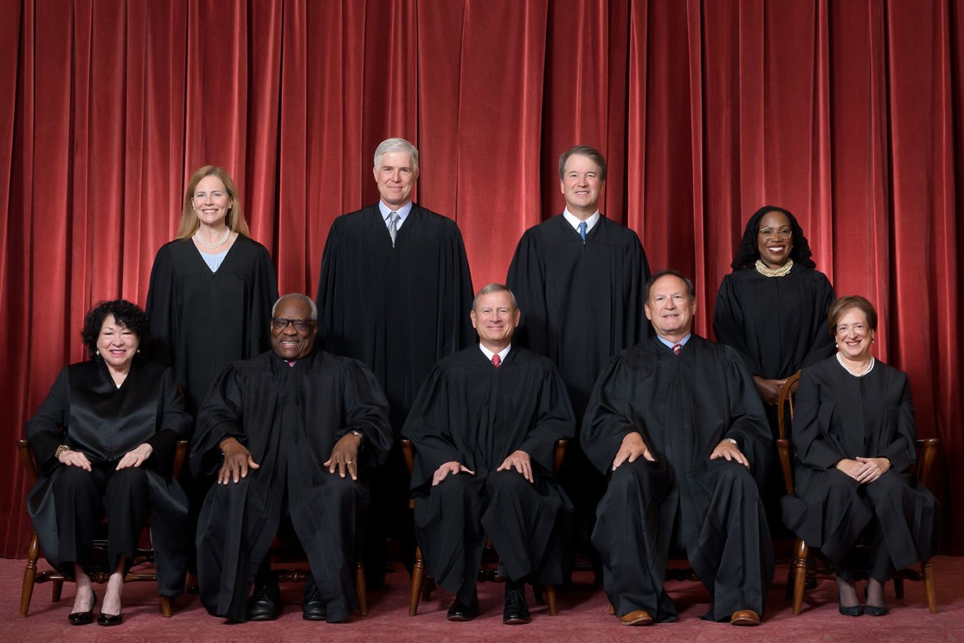 Formal group photograph of the Supreme Court as it was been comprised on June 30, 2022 after Justice Ketanji Brown Jackson joined the Court.  The Justices are posed in front of red velvet drapes and arranged by seniority, with five seated and four standing.Seated from left are Justices Sonia Sotomayor, Clarence Thomas, Chief Justice John G. Roberts, Jr., and Justices Samuel A. Alito and Elena Kagan.
Standing from left are Justices Amy Coney Barrett, Neil M. Gorsuch, Brett M. Kavanaugh, and Ketanji Brown Jackson.Credit: Fred Schilling, Collection of the Supreme Court of the United States
